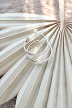 Load image into Gallery viewer, Silver hoop earrings on a palm leaf on a textured beige surface