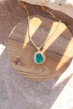 Load image into Gallery viewer, bright green stone against gold pendant with Iines, similar to sun rays. On a piece of driftwood upon a rock.