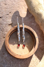 Load image into Gallery viewer, Silver earrings with red stones in a wooden holder on a stone surface