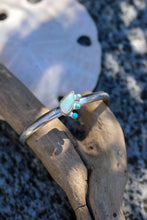 Load image into Gallery viewer, Silver cuff with opal and turquoise stones on a piece of driftwood with a sand dollar in the background