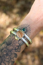 Load image into Gallery viewer, Close-up of a wrist wearing a statement cuff with a brown and green gemstone against a blurred natural background.