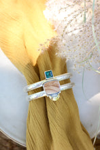 Load image into Gallery viewer, A silver cuff bracelet with Bruneau jasper and blue-green Belgian Fluorite, with gold details, displayed on a yellow fabric.