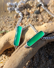 Load image into Gallery viewer, Necklace with green pendant on a piece of driftwood on a beach.