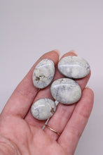 Load image into Gallery viewer, Hand holding four oval-shaped stones with a light gray and white pattern against a plain background
