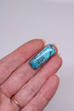 Load image into Gallery viewer, Turquoise stone held between fingers against a plain background
