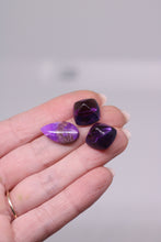 Load image into Gallery viewer, Hand holding three purple gemstones against a neutral background
