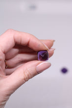 Load image into Gallery viewer, Hand holding a purple gemstone against a plain background
