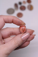 Load image into Gallery viewer, Hand holding a canter opal with a blurred background of various stones
