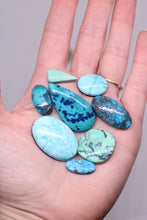 Load image into Gallery viewer, Hand holding a collection of turquoise stones with a gray background
