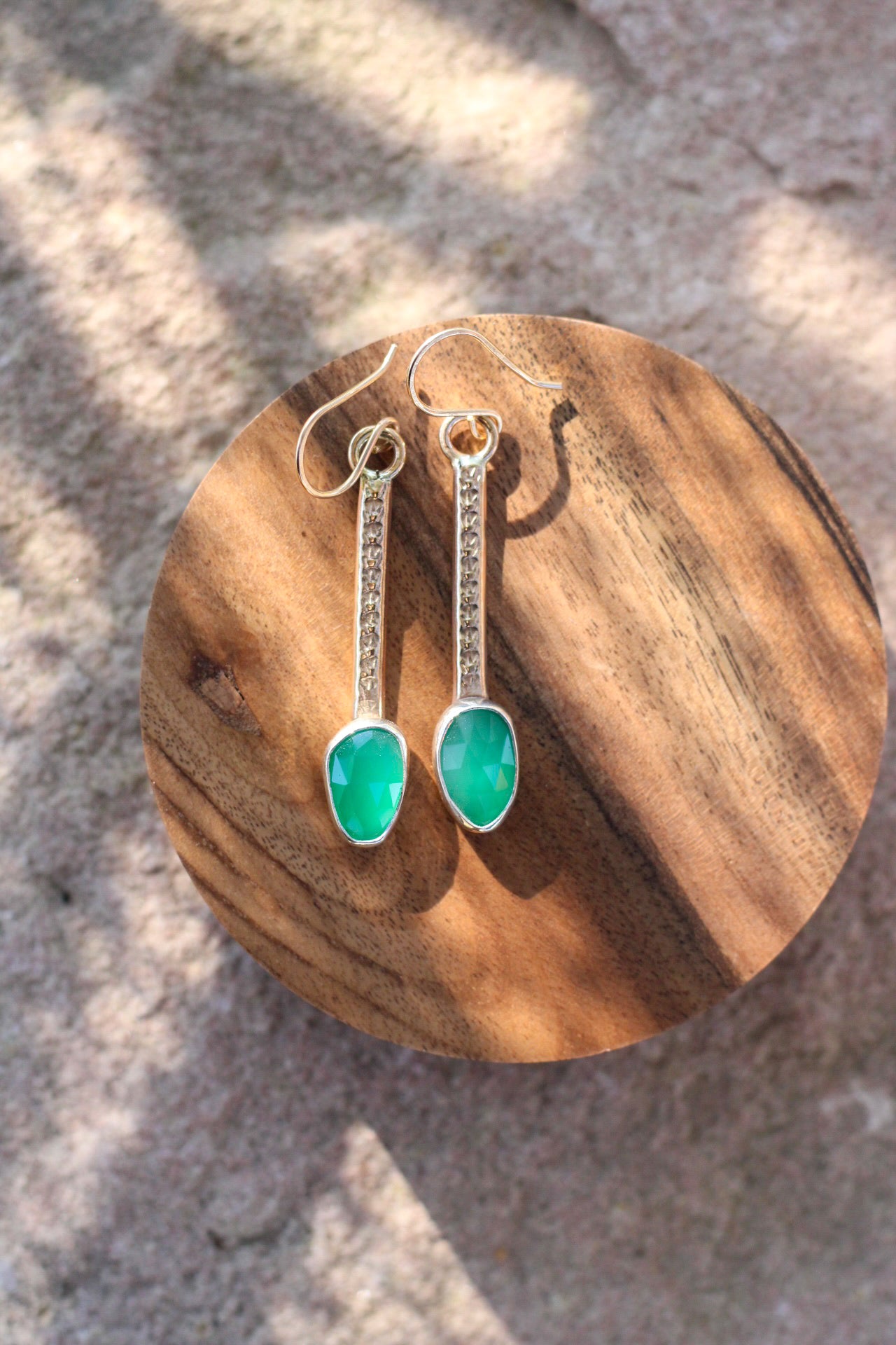 Green teardrop earrings on a wooden stand with a natural stone background