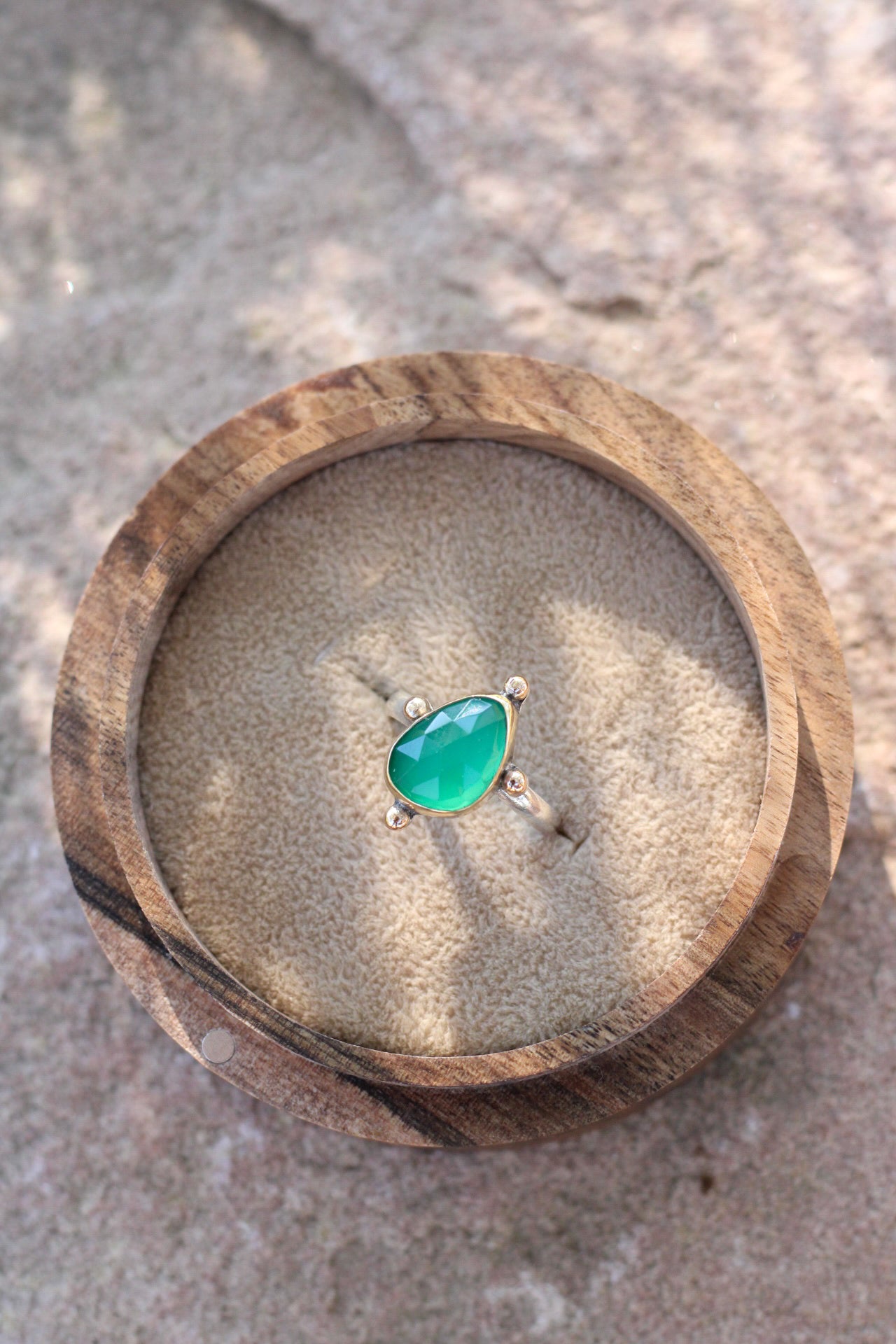 bright green stone in a gold ring in a wooden box on a stone background