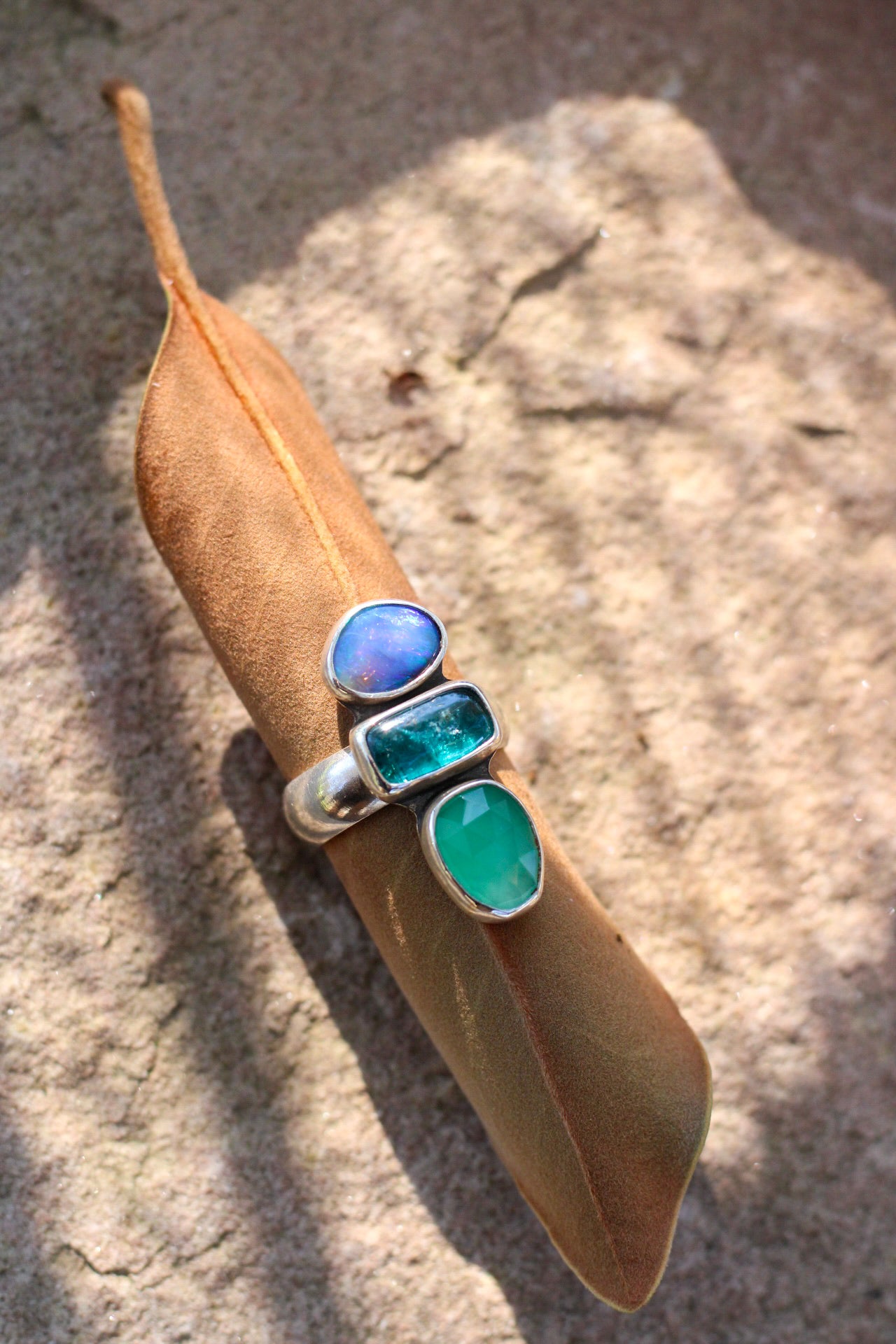 Ring with blue and green stones on a brown leaf against a stone background