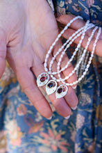 Load image into Gallery viewer, Three pearl necklaces with red gemstone pendants and vintage heart locks held in hands against a floral-patterned fabric background.
