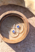 Load image into Gallery viewer, Silver heart-shaped hoop earrings with blue opal stones in a wooden box on a stone surface
