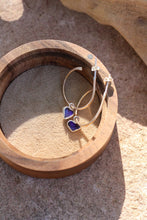 Load image into Gallery viewer, Gold hoop earrings with heart-shaped purple opal stones in a wooden box.
