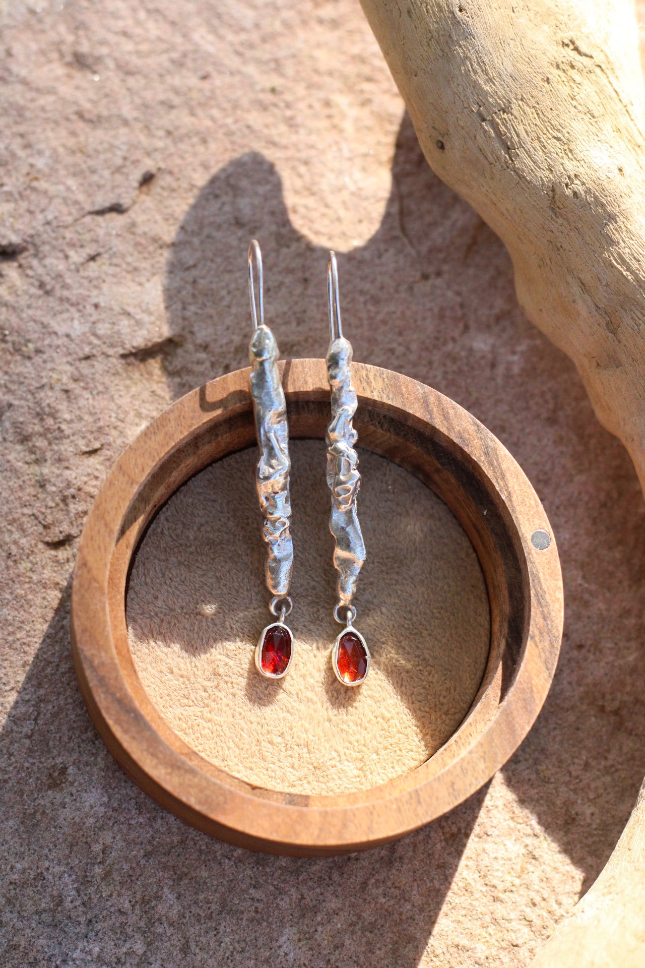 Silver earrings with red stones in a wooden holder on a stone surface