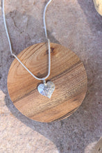 Load image into Gallery viewer, Silver heart-shaped pendant necklace on a wooden coaster
