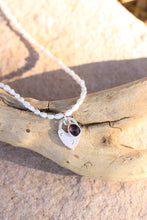 Load image into Gallery viewer, Necklace with a pearl chain, red gemstone pendant, and silver vintage heart lock charm on a wooden surface.
