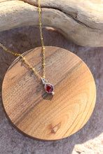 Load image into Gallery viewer, Gold necklace with a red gemstone pendant on a wooden surface
