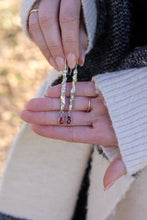 Load image into Gallery viewer, Close-up of hands holding a pair of earrings with red stones with a blurred natural background
