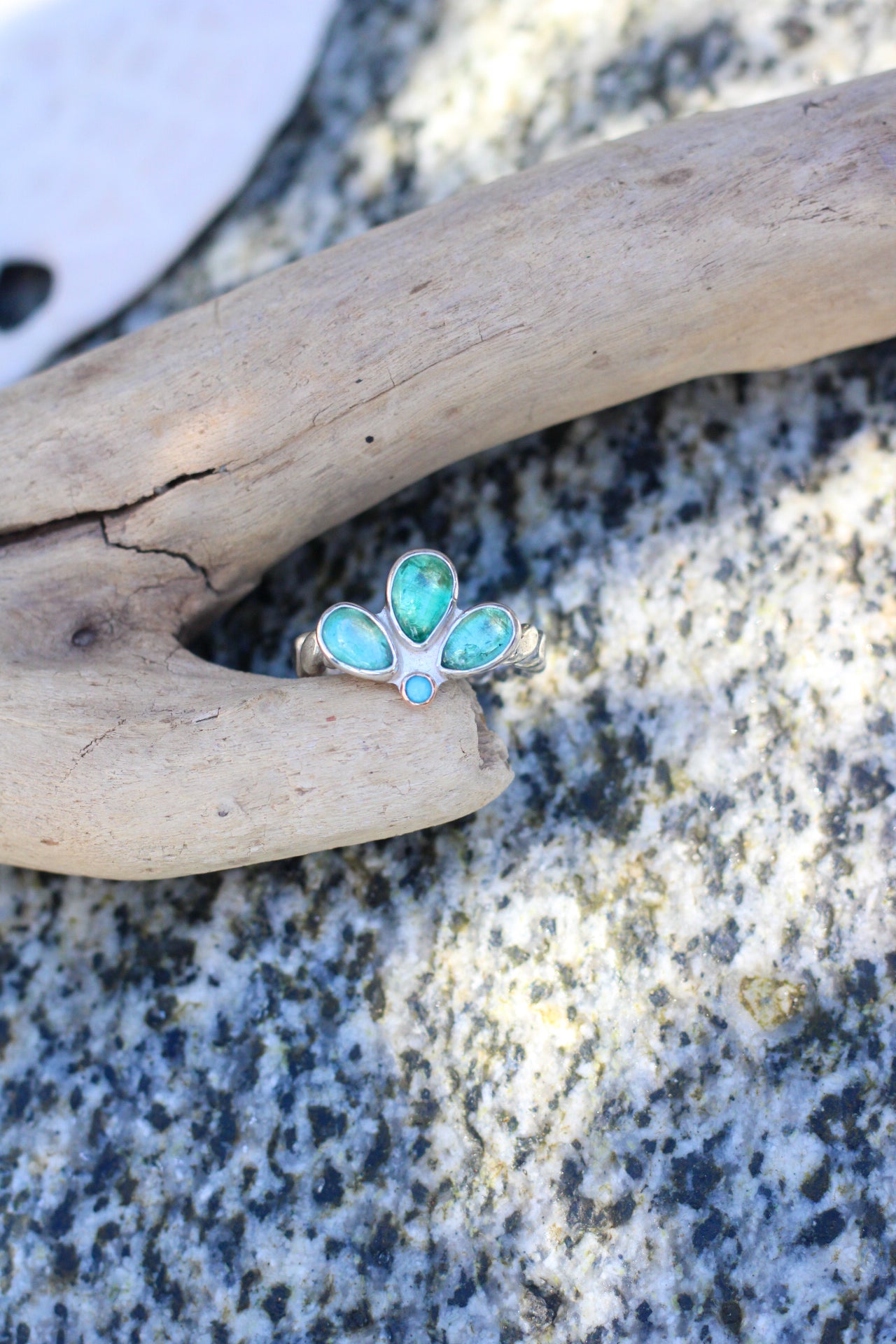 Ring with blue-green stones on a piece of driftwood