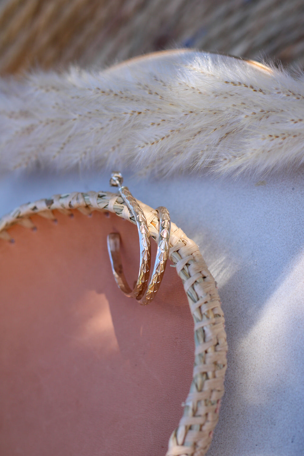 Close-up of a gold stamped hoop earrings with a spring of grass on a textured surface