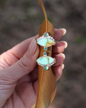 Load image into Gallery viewer, Hand holding a brown leaf with decorative rings featuring turquoise colored stones against a blurred natural background
